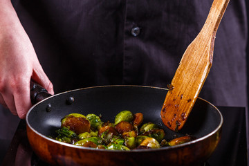 young woman fries Brussels sprouts on a frying pan