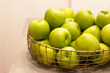 Golden wicker vase with green delicious apples on white background indoors.