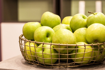 Golden wicker vase with green delicious apples on white background indoors.