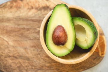 Two halves of avocado in a bowl on a wooden board