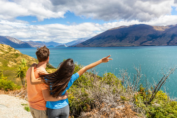 Travel couple enjoying wanderlust road trip in New Zealand, woman with arm up in excitement at Lake view in NZ. Trampers traveling summer destination landscape.
