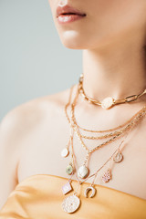 cropped view of young woman with shiny lips in golden necklaces isolated on grey