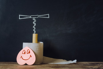 Constipation concept. Roll of toilet paper and a corkscrew on the background of chalk board