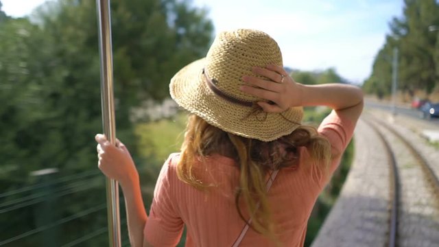 A young woman wearing straw hat enjoying traveling on an old tram or train, admiring beautiful southern tourist locations, feeling excited and happy