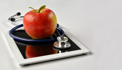 Medical stethoscope and red apple lying on a tablet isolated on white background. Medical content. Portable electronic device. Gadget. Copy space for your text. Close up photo.