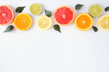 Colorful fruit border of fresh citrus slices with leaves. Top view, flay lay over a white background with copy space.