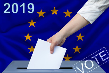 Female hand puts down a white sheet of paper with a mark as a symbol of a ballot paper against the background of the flag of the European Union, the symbol of a parliamentary elections.