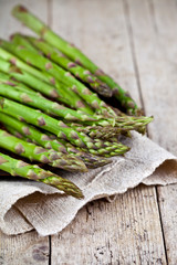 Bunch of fresh raw garden asparagus closeup and linen napkin on rustic wooden table background.