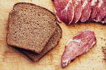 Smoked meat, pepper. Slices of smoked meat with black bread on a wooden board.