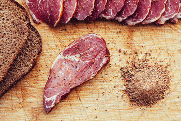 Smoked meat, pepper. Slices of smoked meat with black bread on a wooden board.