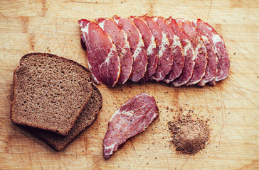 Smoked meat, pepper. Slices of smoked meat with black bread on a wooden board.