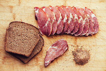 Smoked meat, pepper. Slices of smoked meat with black bread on a wooden board.