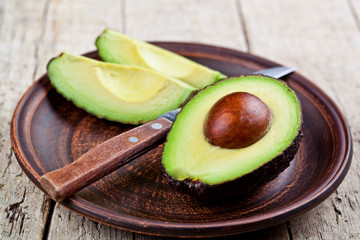 Fresh organic avocado on ceramic plate and knife on rustic wooden table background.