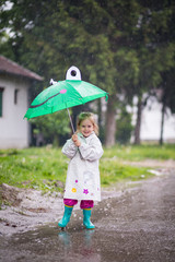 Happy child playing in the rain. Little girl with umbrella having fun outdoor .