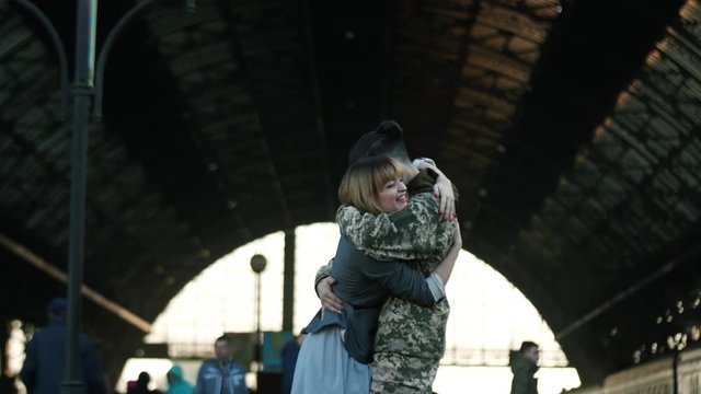 Happy Caucasian soldier throws his backpack to embrace his beloved girlfriend, wife, sister on a railway station. Army soldier returning home to the embrace of his wife. True love, happy reunion