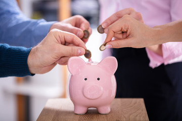 People Inserting Coins Into Piggybank