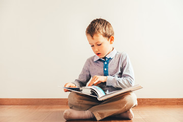 Boy sitting on the floor with reading a book on his knees, isolated on white background.