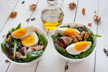 Fototapeta Sałatka z jajkiem, orzechami i szynką parmeńska w białych miskach, w tle oliwa z oliwek obraz