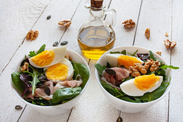 Salad with egg, walnuts and parma ham in white bowls, olive oil in the background
