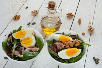 Sałatka z jajkiem, orzechami i szynką parmeńska w białych miskach, w tle oliwa z oliwek