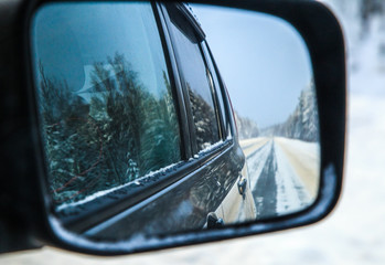 Naklejka premium Winter forest highway at the automobile rear-view mirror