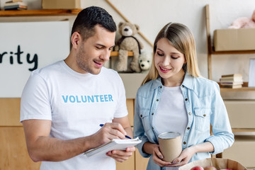 handsome young volunteer writing in notebook while standing near pretty blonde woman