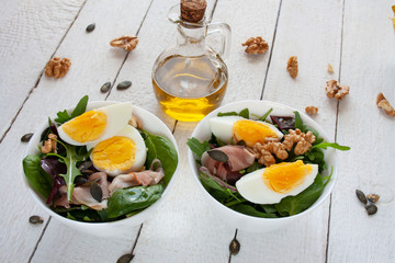 Fototapeta na wymiar Sałatka z jajkiem, orzechami i szynką parmeńska w białych miskach, w tle oliwa z oliwek