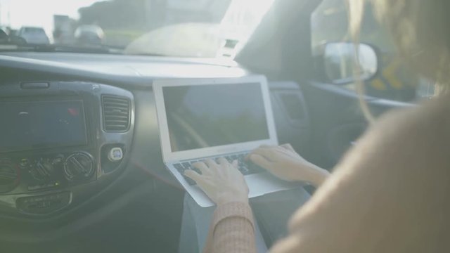 Woman using laptop in car. Cropped shot of young blonde woman sitting in car and typing on laptop computer. Transportation concept