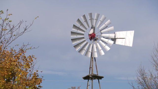 Top of a windmill barely moving with trees beside