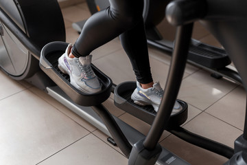 Female legs in white sneakers work on the stepper simulator of a sports studio. Woman at workout in...