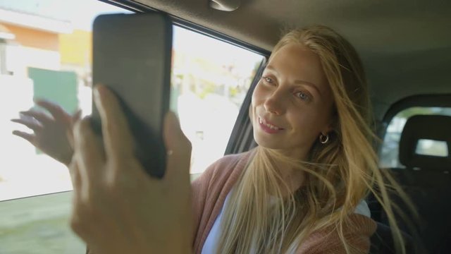 Happy girl taking selfie in car. Beautiful smiling young woman sitting in car and photographing with smartphone. Technology concept