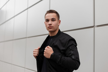 Attractive handsome young man in a black fashionable jacket with a stylish hairstyle is standing...