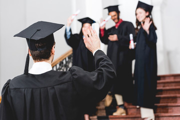 selective focus of student in graduation cap waving hand