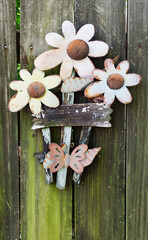 Weathered and rusty metal flowers and butterfly ornament mounted on fence with mildew.