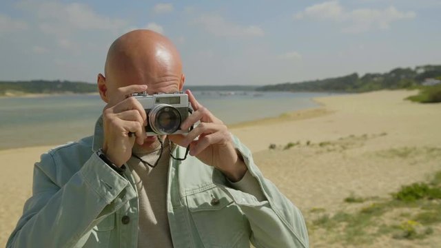 Man holding camera and photographing on beach. Handsome happy young man taking pictures with photo camera on sandy beach. Photography concept
