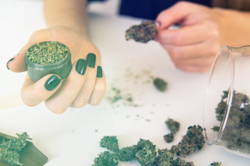 Close up of marijuana blunt with grinder. Woman rolling a cannabis blunt on white background. Woman...