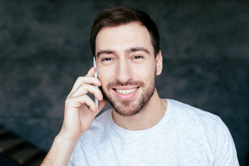 front view of smiling bearded man talking on smartphone and looking at camera
