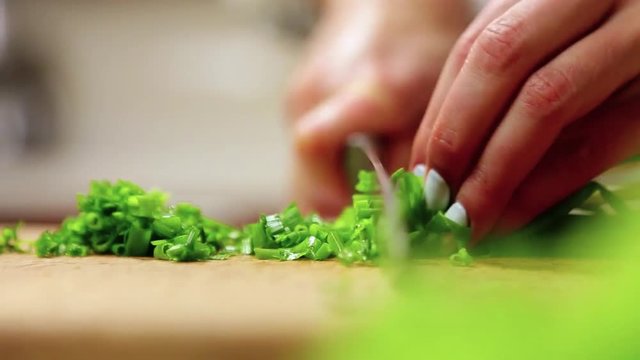 Close up rotation view of female hands professionally slicing cutting the green onion on the cutting board. Vegetables and fresh greens, vegetarian food, delicious flavor. Healthy lifestyle
