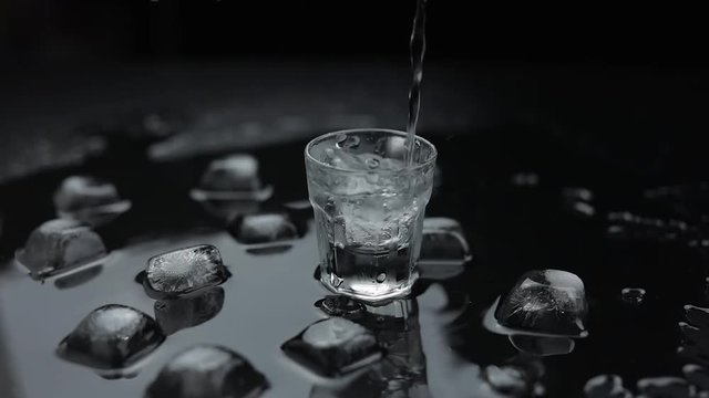 Pouring up shot of vodka into glass. Black background. Pour of alcohol drink