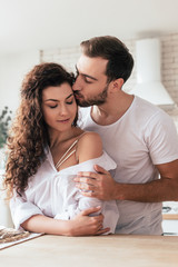 bearded man embracing and kissing girlfriend in kitchen