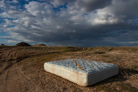 Discarded bed mattress in dirt road setting in front of hills and cloudy panoramic sky