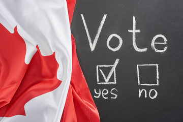 Fototapeta na wymiar top view of vote lettering and check mark near yes word on black chalkboard near flag of Canada