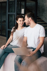 smiling couple with laptop sitting on sofa and looking at each other
