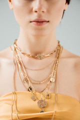 partial view of young woman with shiny lips in golden necklaces isolated on grey