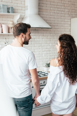 back view of couple holding hands and looking at each other in kitchen