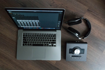 Flat lay of sound designers tools on dark wood table: laptop with mixing scene, sound card, headphones, microphone. Sound engineering tools. Professional sound card for music mixing and mastering