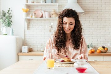 charming curly girl looking at pancakes with smile