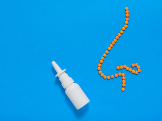 The nasal spray and the figure of a nose of orange pills on a blue background. The concept of treatment of diseases of the nose and allergies. Flat lay.