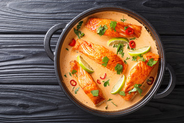 Tender salmon fillet in spicy Thai coconut curry with lime and herbs close-up in a pan. horizontal top view - obrazy, fototapety, plakaty