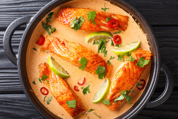 Fillet salmon in spicy Thai coconut sauce with lime and herbs close-up in a pan. horizontal top view
